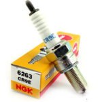 القلاف_للدراجات_النارية_ تظهر شمعة احتراق (بوجي) واحدة من طراز NGK CR9E أمام علبتها الصفراء والحمراء التي تحمل الرقم 6263 CR9E. _دراجة_نارية